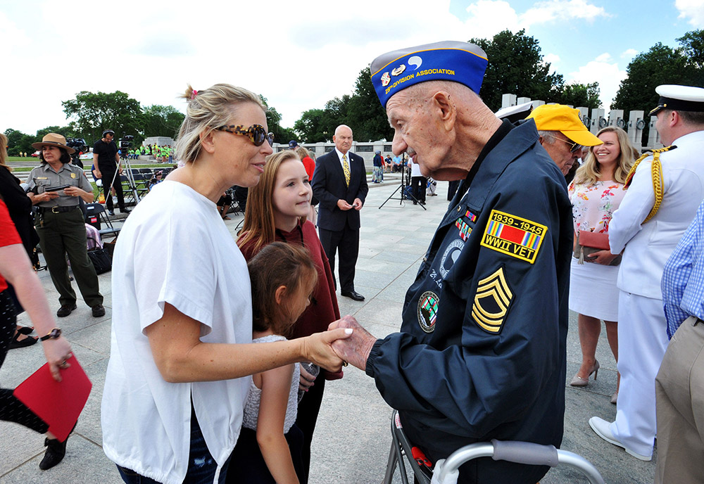 veteran World War II Veteran speaking with a mother and two daughters at the World War II monument in Washington, DC.